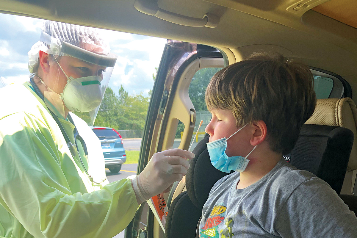 A boy in a car gets a COVID-19 test by a medical worker in full PPE