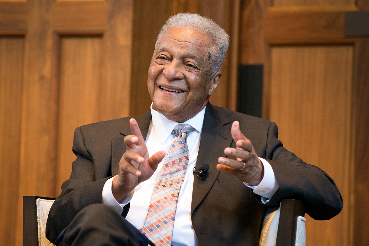 Photograph of Dr. Gerald Hood gesturing with both hands while talking onstage during an event honoring him at Emory University.