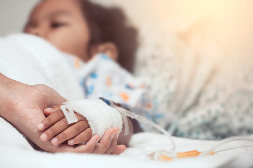 an unseen person holds the hand of a hospitalized child